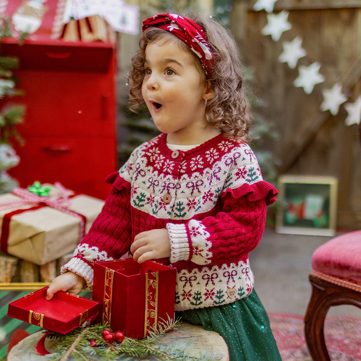 Fillette émerveillée découvrant un cadeau de Noël, vêtue d’un chandail rouge et blanc en tricot festif, collection Souris Mini.