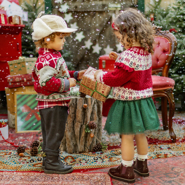 Deux enfants vêtus de chandails en tricot festifs s’échangent un cadeau dans un décor de Noël magique, collection Souris Mini.